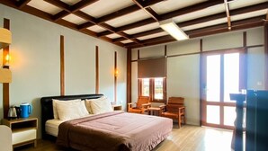 A hotel room with a bed, wooden floor, a desk, a chair, a window, and a door. - Oase Resort Bandung (Parongpong)