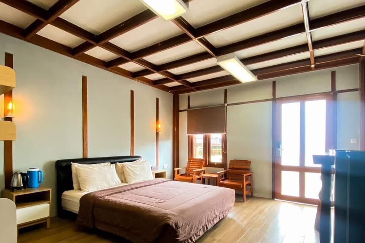 Een hotelkamer met een bed, houten vloer, bureau, stoel, raam en deur.