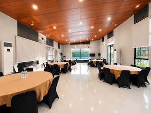 A conference room with round tables, black chairs, a wooden ceiling, and large windows. - Oase Resort Bandung (Parongpong)