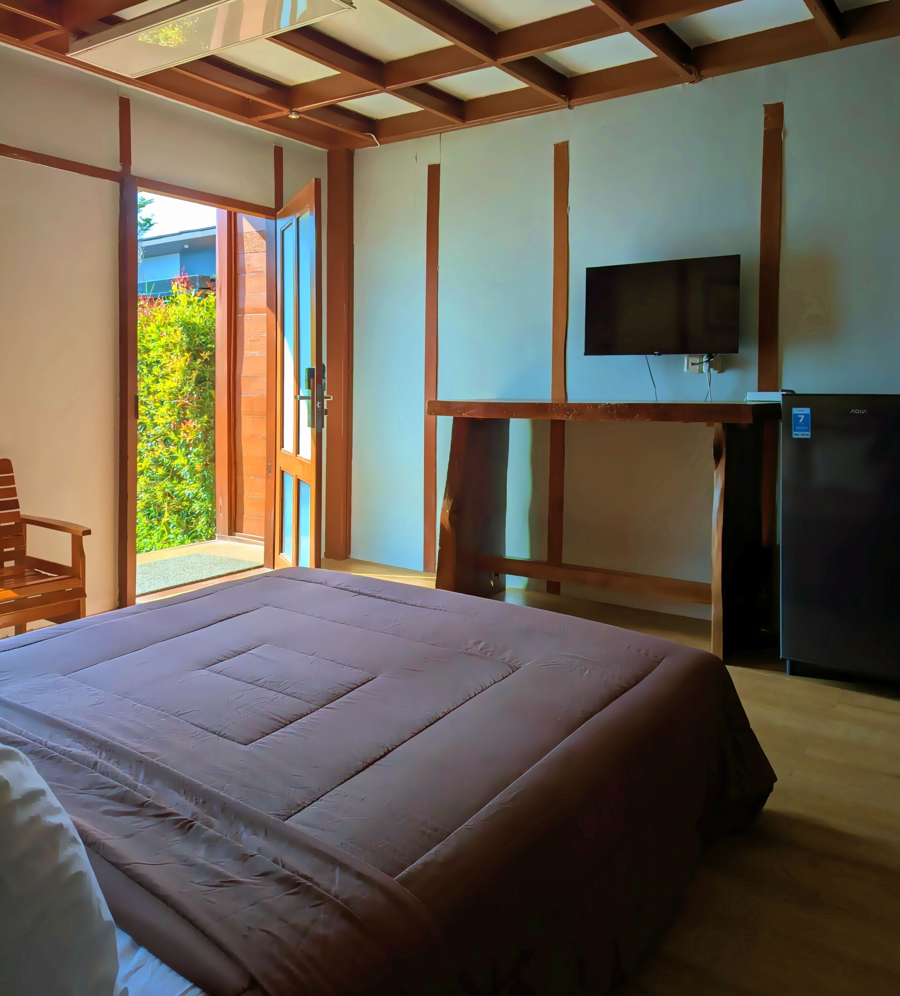 A bedroom with a bed, a television mounted on the wall, and a refrigerator.