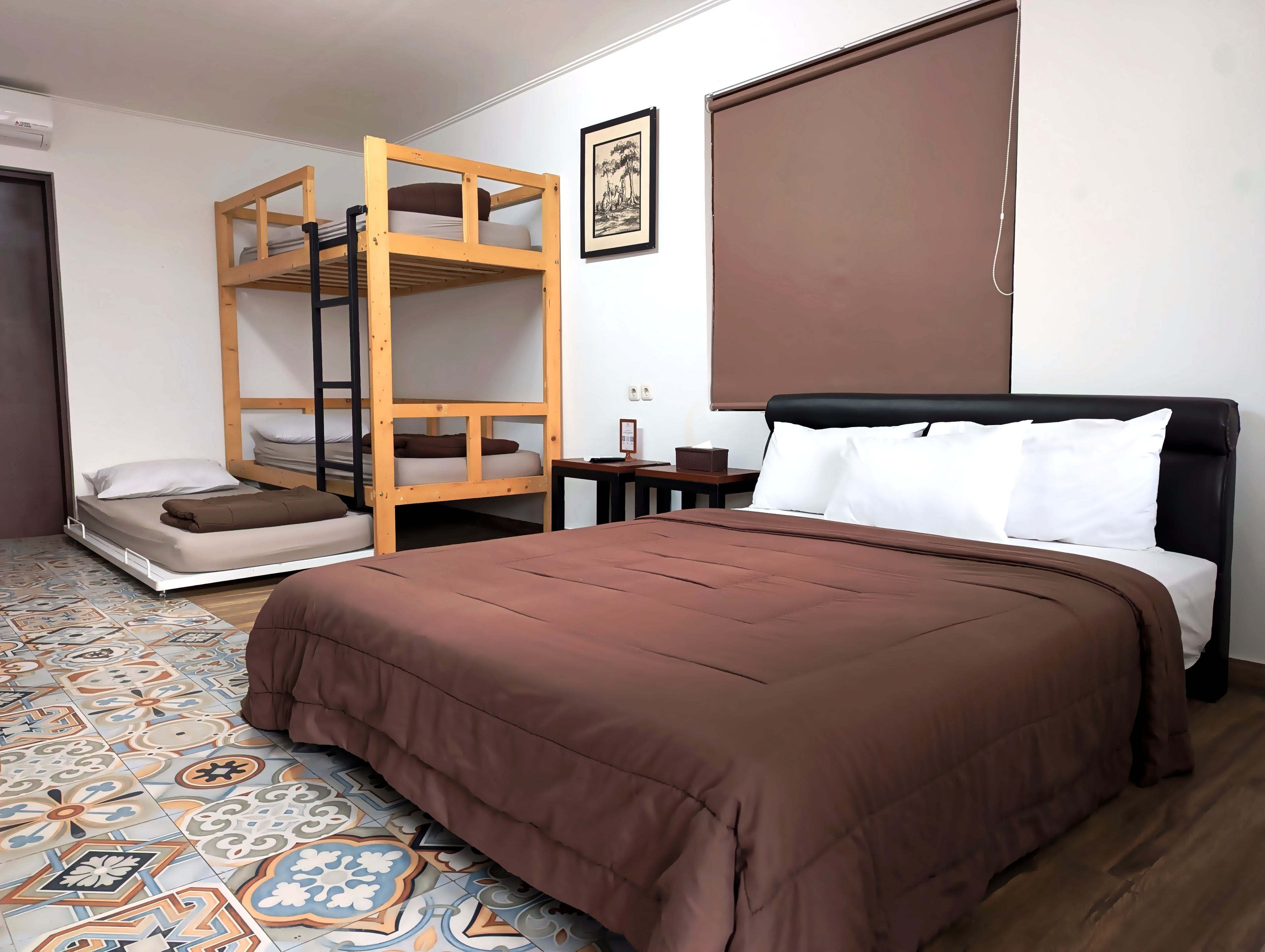 Una habitación con literas, una cama individual, piso estampado, un cuadro en la pared y una ventana con persiana.