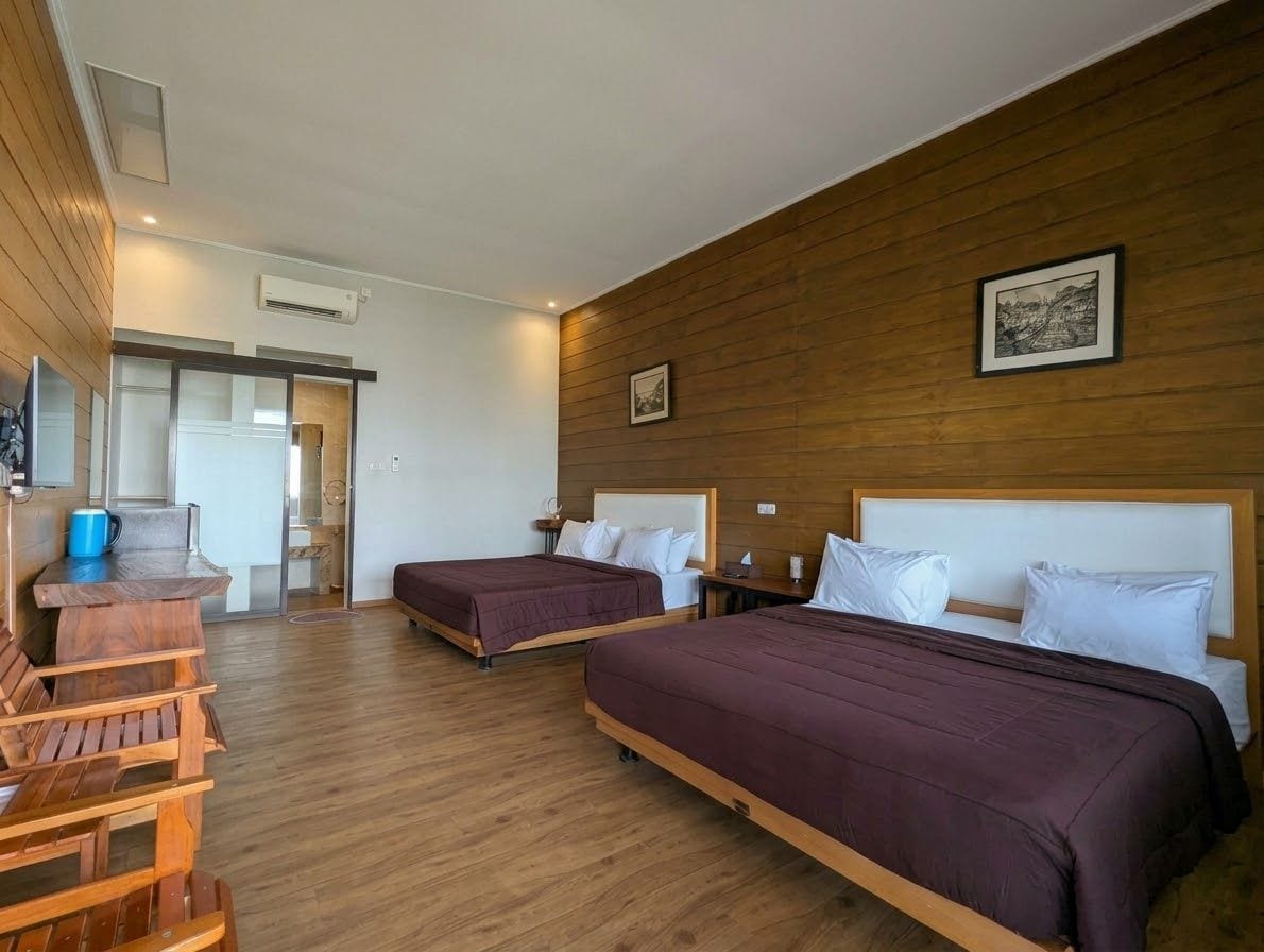 A hotel room with two beds, wooden flooring, a wooden wall panel, a small table, and a picture on the wall.