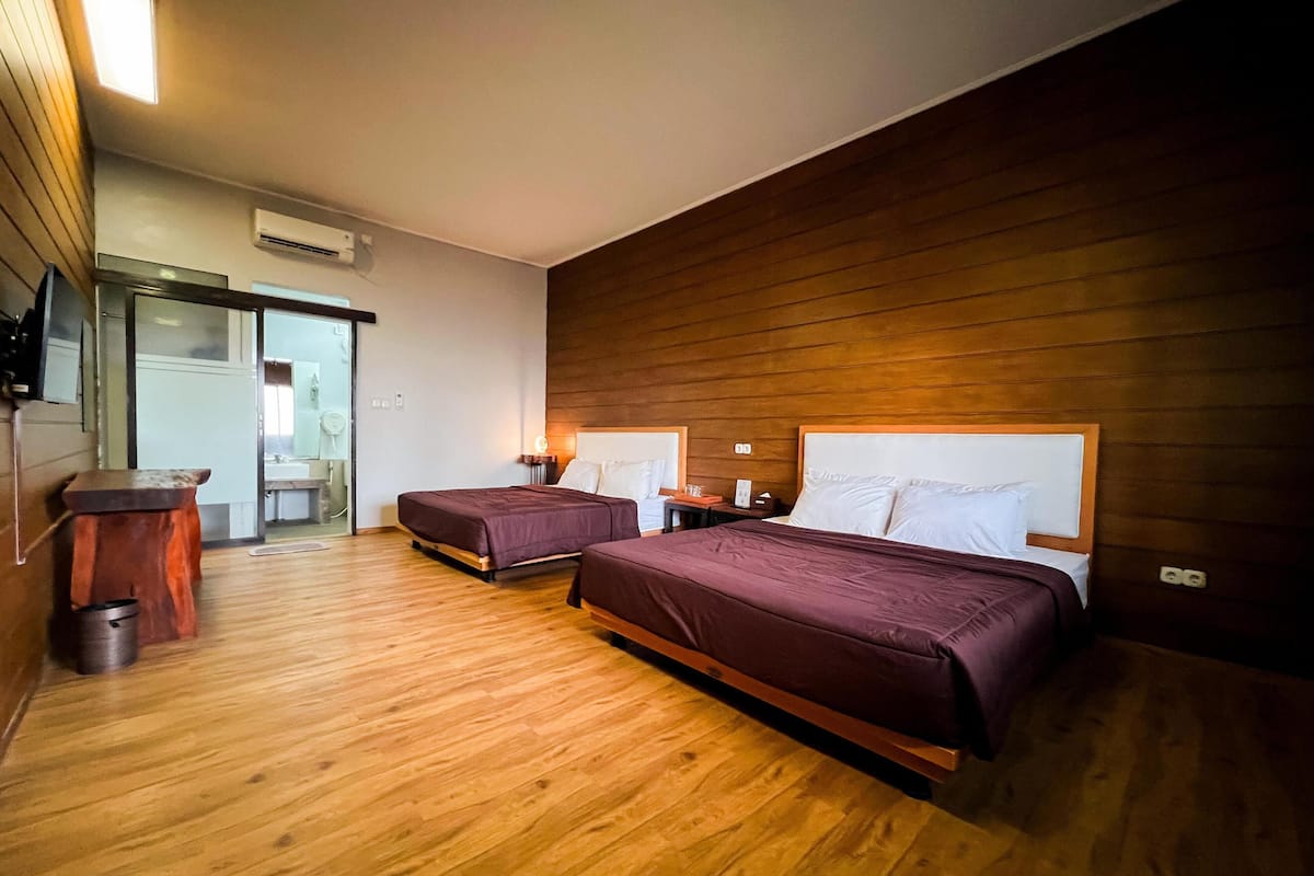 Een hotelkamer met twee bedden, houten vloeren, een klein bureau en een badkamer zichtbaar door een schuifdeur.