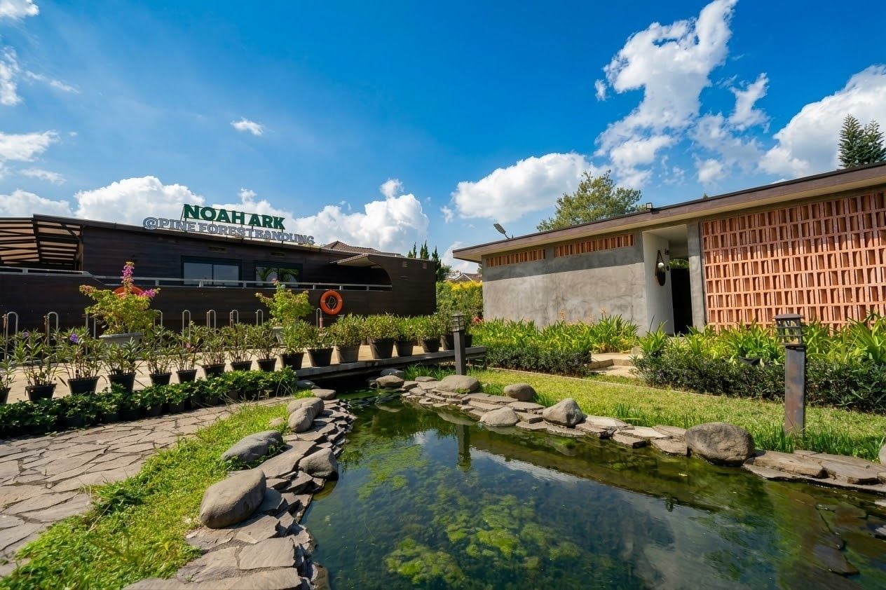 Un edificio con un letrero que dice 'NOAHARK PINE FOREST RESORT' y un pequeño estanque con rocas y plantas.