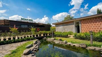 Un edificio con un letrero que dice 'NOAHARK PINE FOREST RESORT' y un pequeño estanque con rocas y plantas.