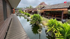 A wooden deck overlooking a water feature with potted plants and traditional-style buildings. - Oase Resort Bandung (Parongpong)