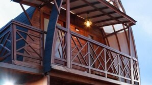 A wooden cabin with a balcony, a small porch, and a light fixture on the front door. - Oase Resort Bandung (Parongpong)