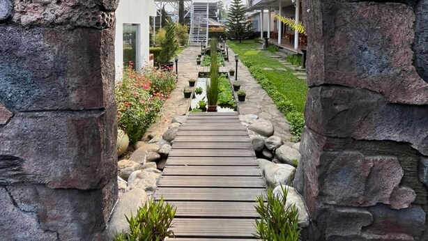A stone archway leading to a wooden pathway with potted plants. - Oase Resort Bandung (Parongpong)