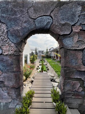 A stone archway leading to a wooden pathway with potted plants. - Oase Resort Bandung (Parongpong)