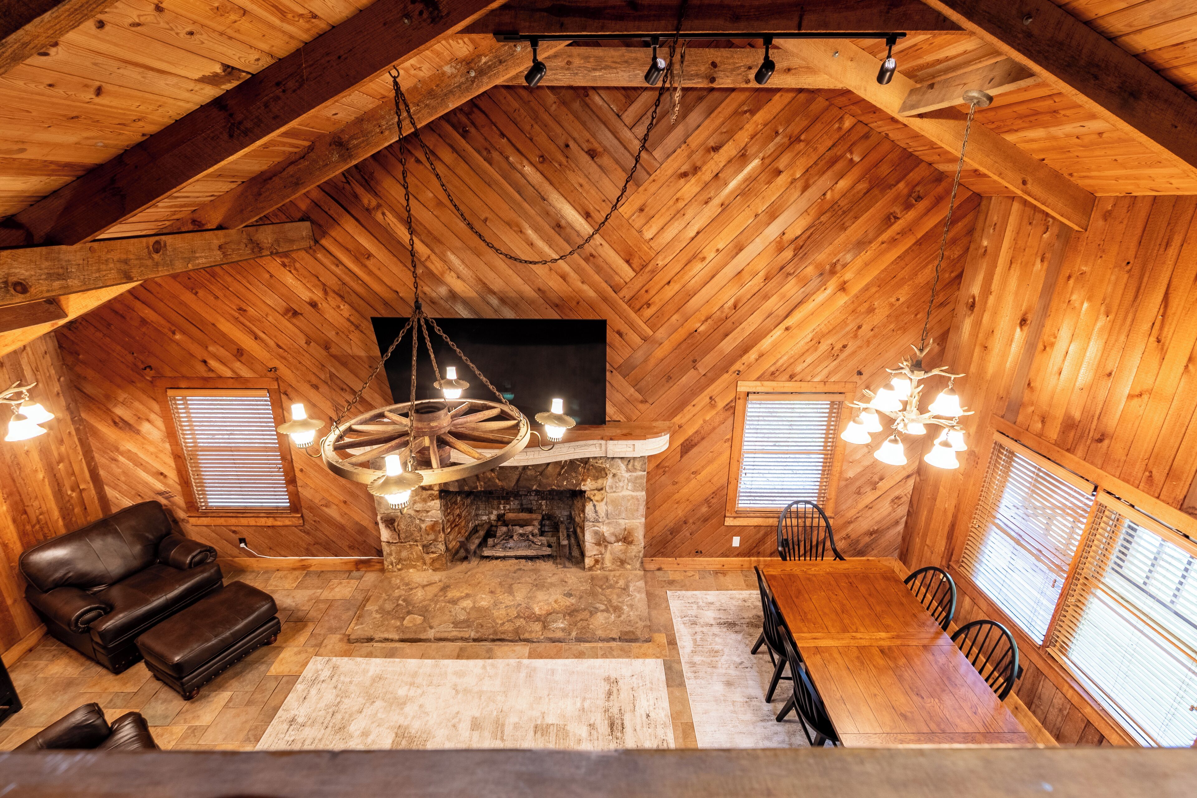 A rustic wooden interior with a stone fireplace, leather sofa, dining table, and chairs.