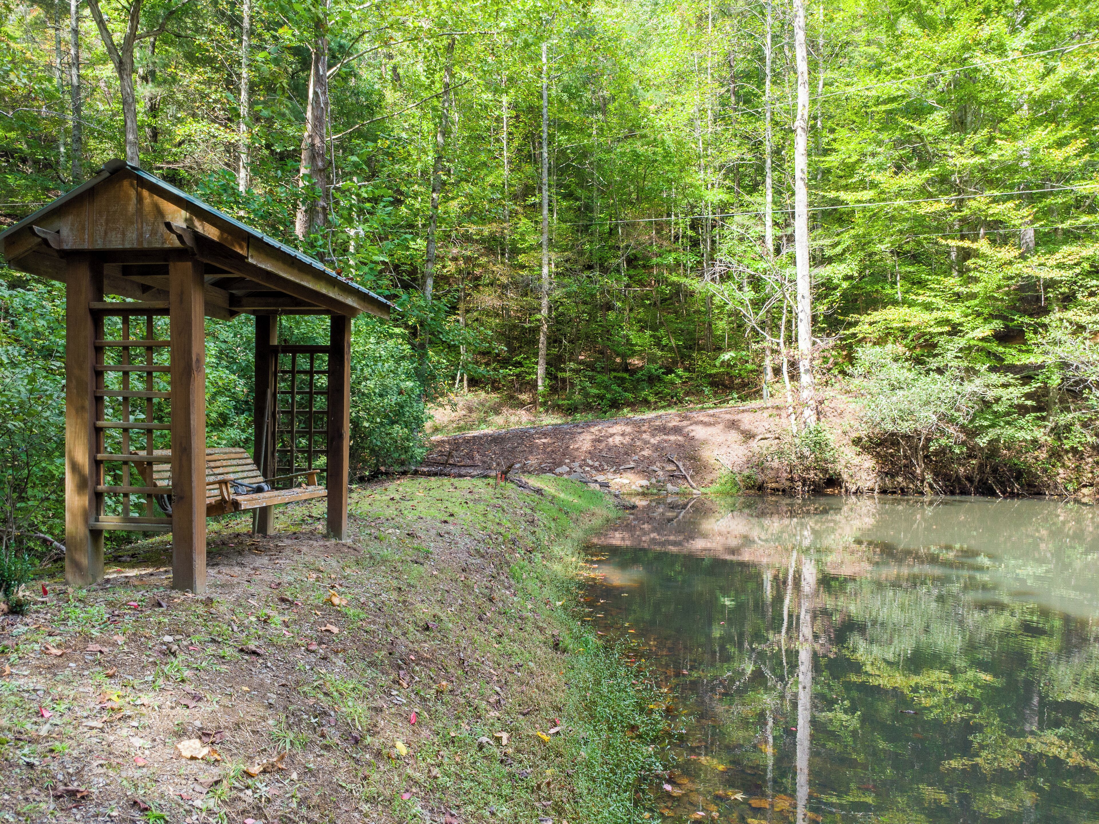 A wooden gazebo with a bench, surrounded by a forest and a calm pond.
