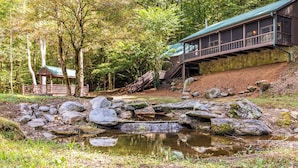 A rustic cabin with a stone exterior, a wooden deck, and a small pond with rocks.