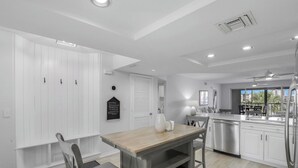 A modern kitchen with white cabinetry, a wooden dining table, and a built-in oven. - Bayfront Bliss Near Vanderbilt Beach (Naples)