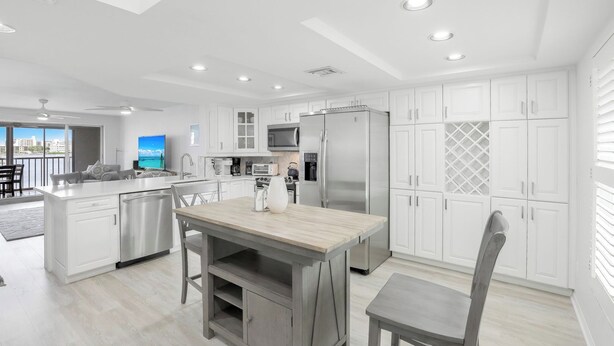 A modern kitchen with white cabinetry, a stainless steel refrigerator, and a dining area with a wooden table and chairs. - Bayfront Bliss Near Vanderbilt Beach (Naples)