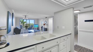 Cozinha moderna com uma bancada grande, armários brancos e vista para o exterior.
