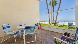 A covered patio with a table and chairs, a red exercise ball, and a view of the beach with lounge chairs. - Combined Beachfront Bliss - Aloha Kai #24 & #24N - Roelens (Siesta Key)
