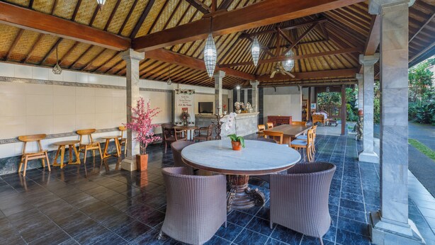An outdoor covered area with a round table and chairs, a bar, and a view of the garden. - Griya Agung Guesthouse Ubud (Ubud)