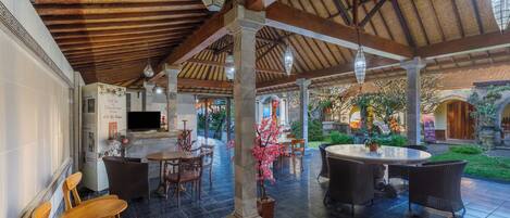 An indoor patio area with a tiled floor, wooden furniture, and a thatched roof ceiling.