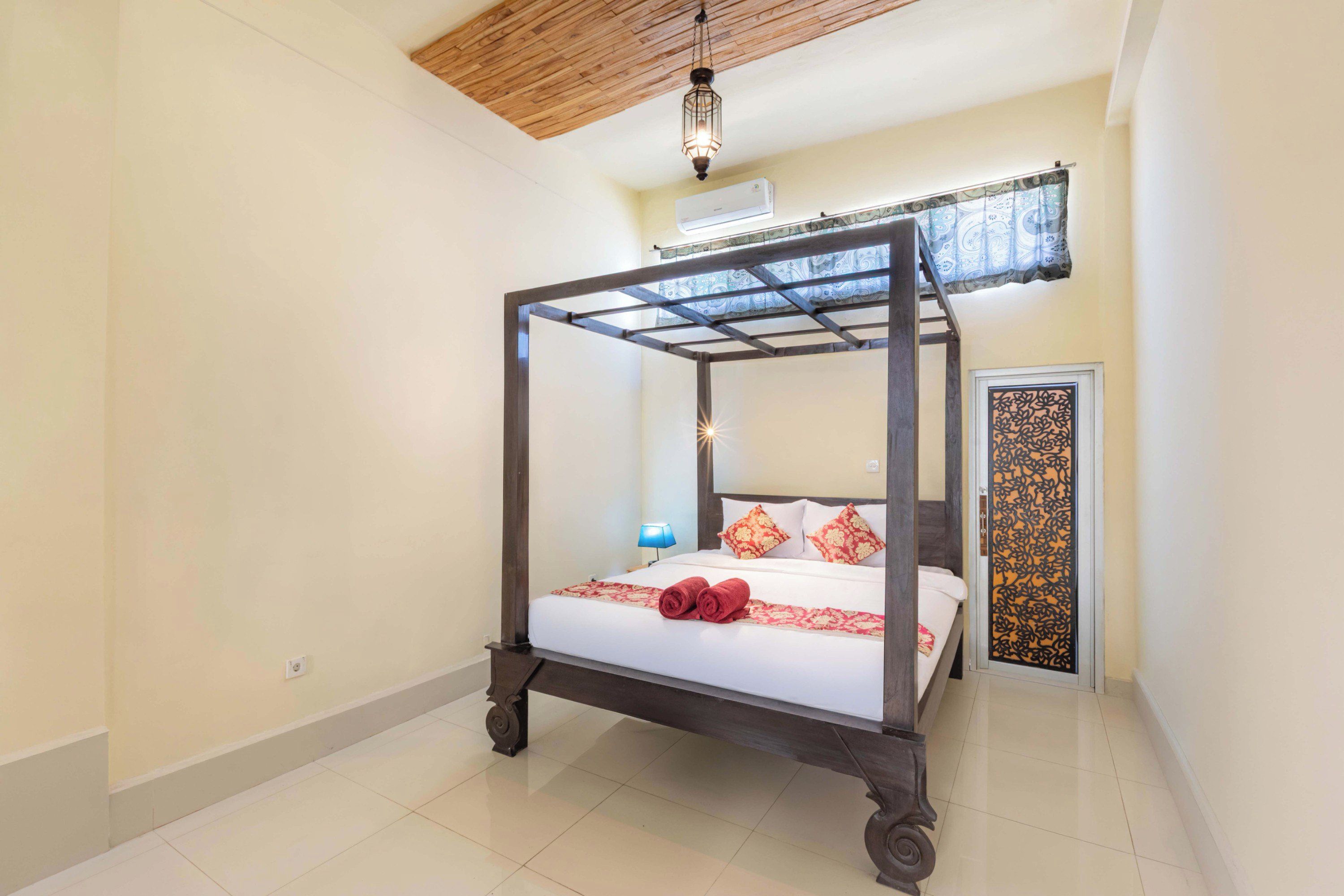 A four-poster bed with a wooden frame, white bedding, and red decorative pillows.