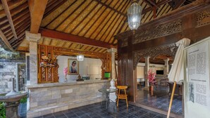 A reception area with a stone counter, a Buddha statue, and a traditional wooden ceiling. - Griya Agung Guesthouse Ubud (Ubud)