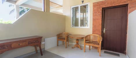A room with a desk, two chairs, a small table, a window, and a door.