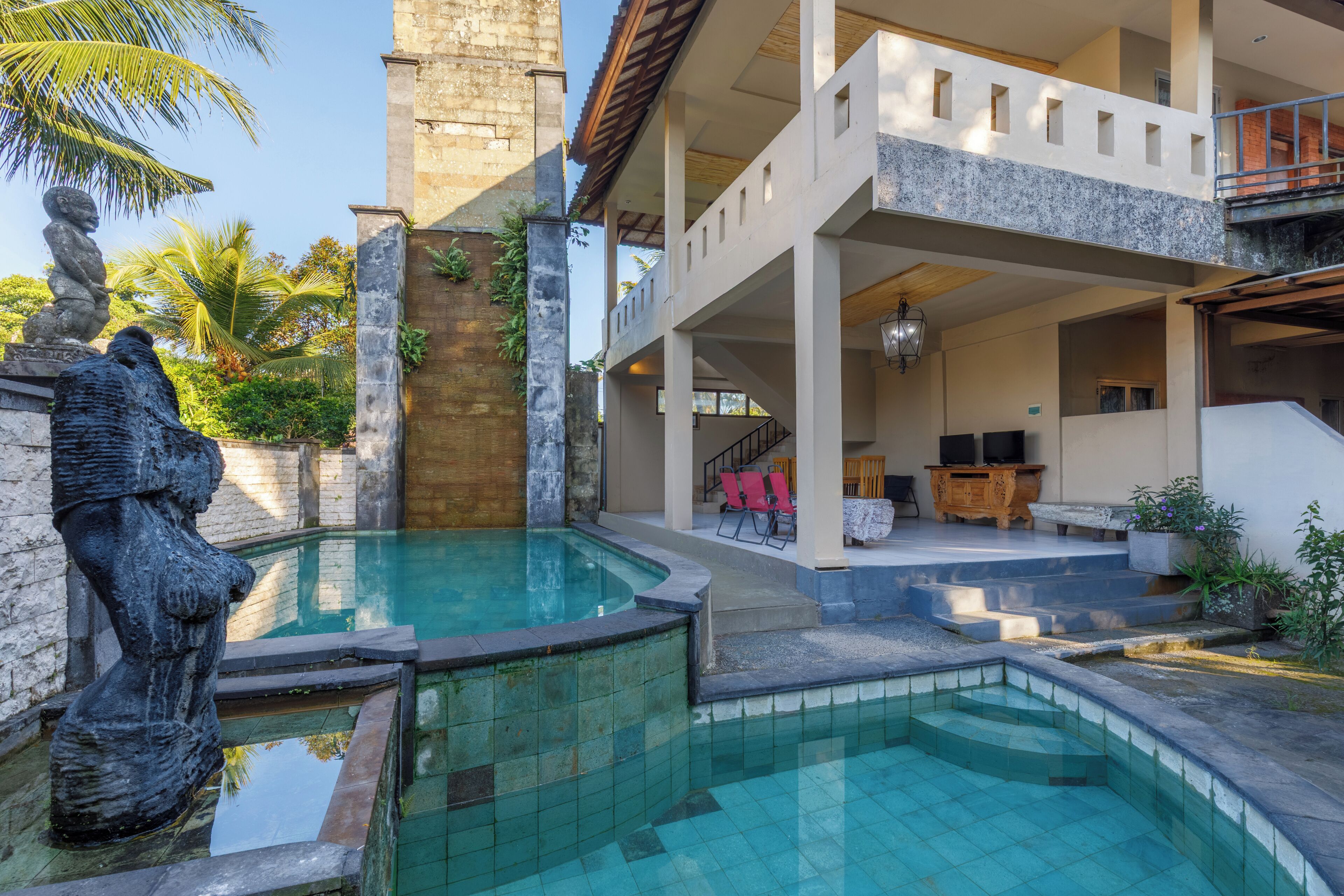 Zona de piscina con una estatua de piedra, una escalera y un área de descanso con mesa y sillas de madera.