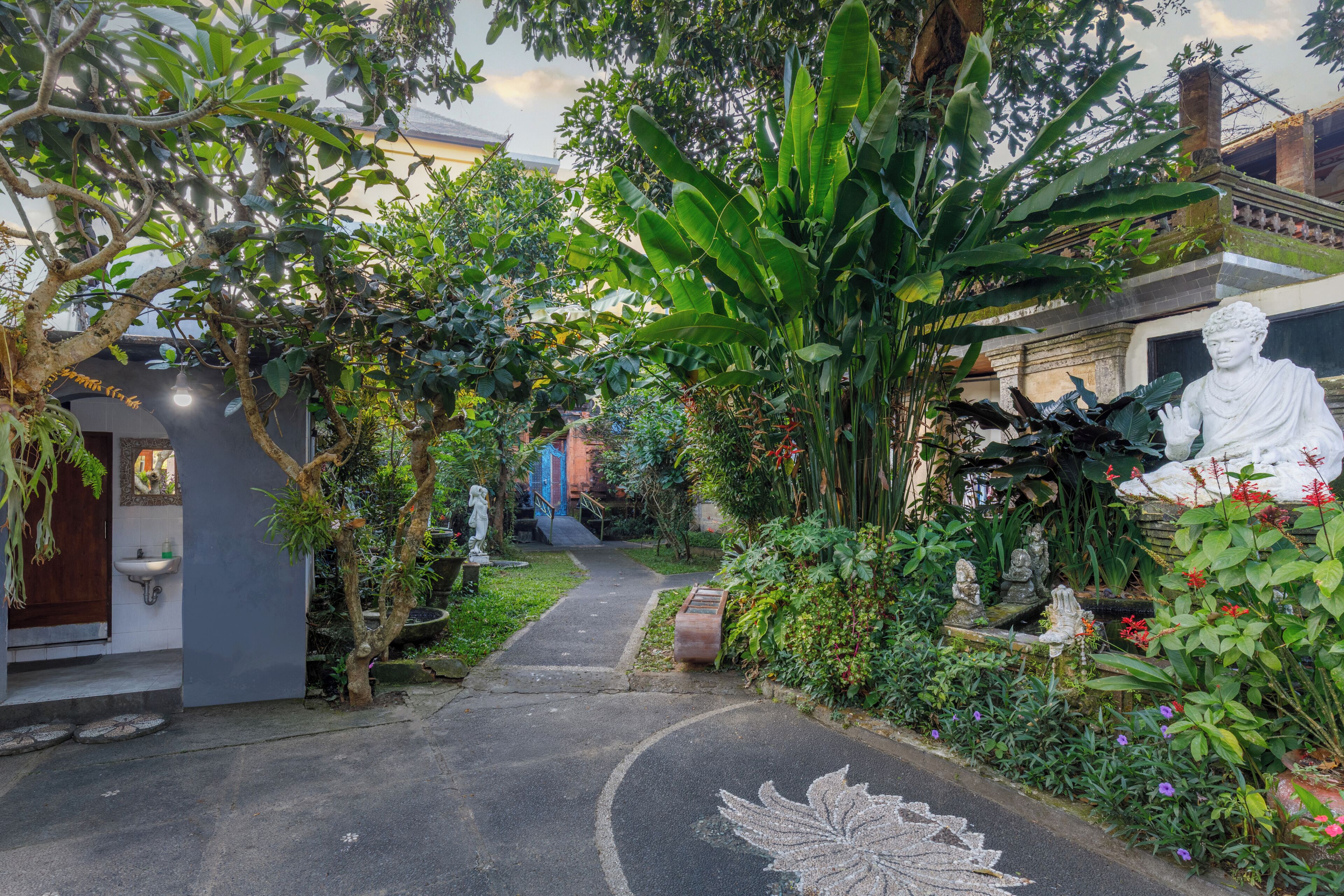 Uma trilha no jardim leva a um edifício com uma estátua e muita vegetação.
