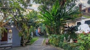 A garden pathway leading to a building with a statue and lush greenery. - Griya Agung Guesthouse Ubud (Ubud)
