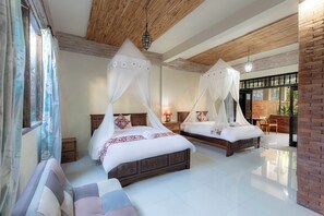 A hotel room with two beds, each with a canopy, a sitting area with a sofa, and a view of the outdoors. - Griya Agung Guesthouse Ubud (Ubud)