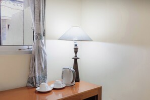 A room with a wooden table, a white electric kettle, a white cup and saucer, a lamp, and a curtain. - Griya Agung Guesthouse Ubud (Ubud)