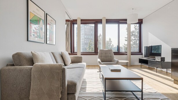 Ein modernes Wohnzimmer mit einer Couch, einem Sessel, einem Couchtisch und einem Flachbildfernseher.