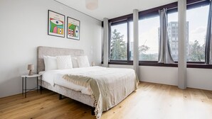 Ein Schlafzimmer mit einem großen Bett, einem Nachttisch, einer Lampe und zwei gerahmten Kunstwerken an der Wand.