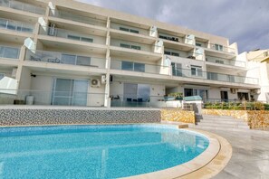 A modern multi-story building with a swimming pool in front.