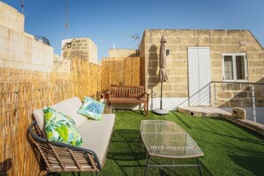 Eine Terrasse mit Korbstuhl, Sofa und Glastisch.