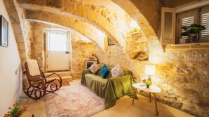 Una habitación acogedora con paredes de piedra, un sillón de madera, un sofá verde y una mesita con lámpara.