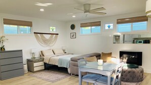 Een moderne, goed verlichte slaapkamer met een bed, nachtkastjes, een bureau met stoel, een plafondventilator en een groot raam met jaloezieën.