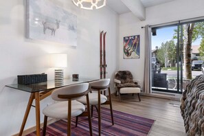 Une chambre moderne avec une table en verre, deux chaises, une lampe, un tableau sur le thème du ski et une vue sur l’extérieur.