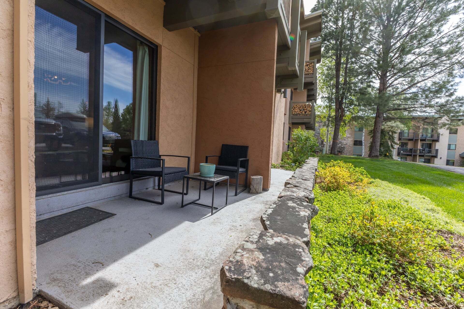 A building with a covered outdoor seating area, a large window, and a stone planter with greenery.