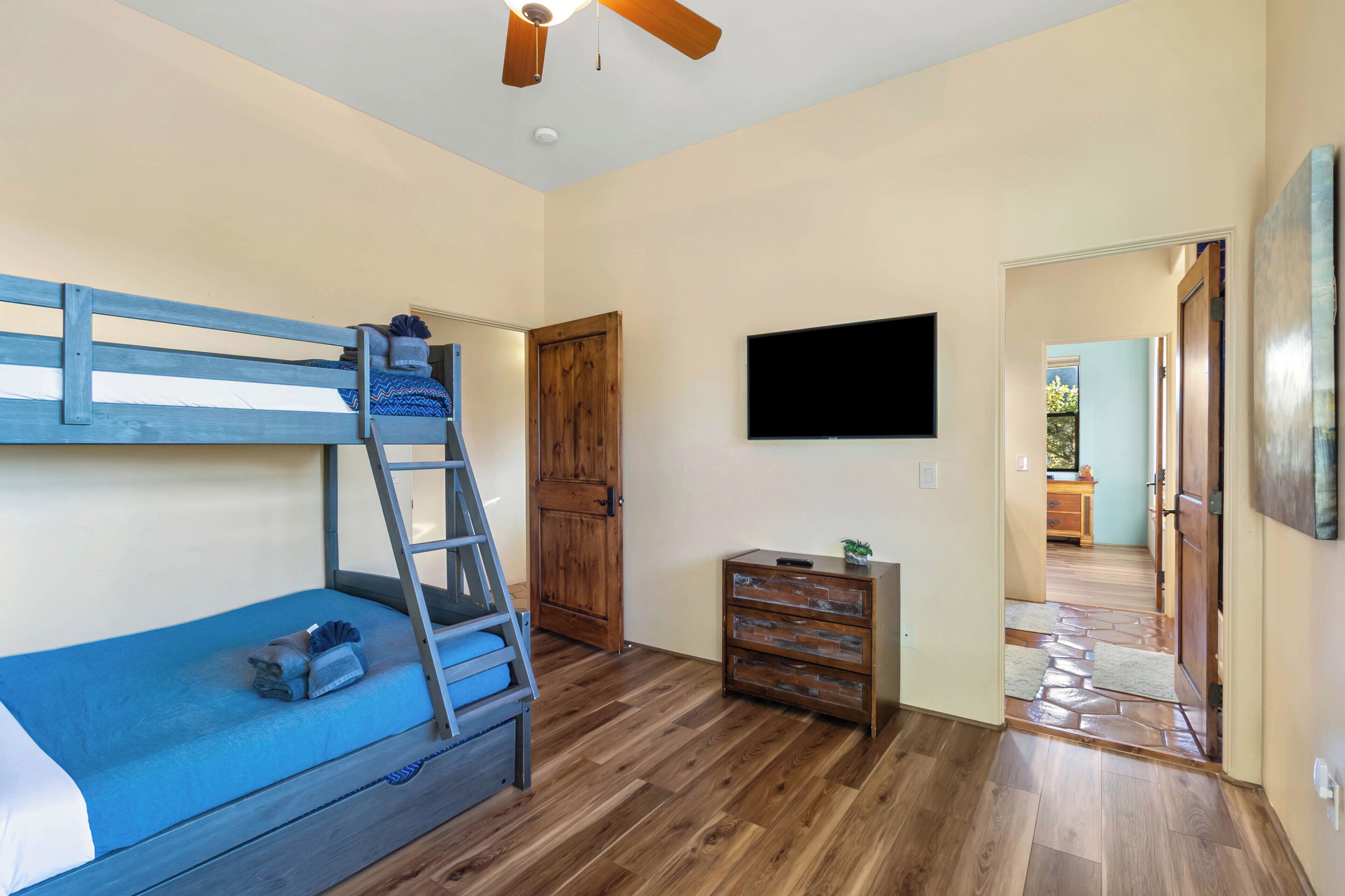 A bedroom with a bunk bed, wooden dresser, and a television mounted on the wall.