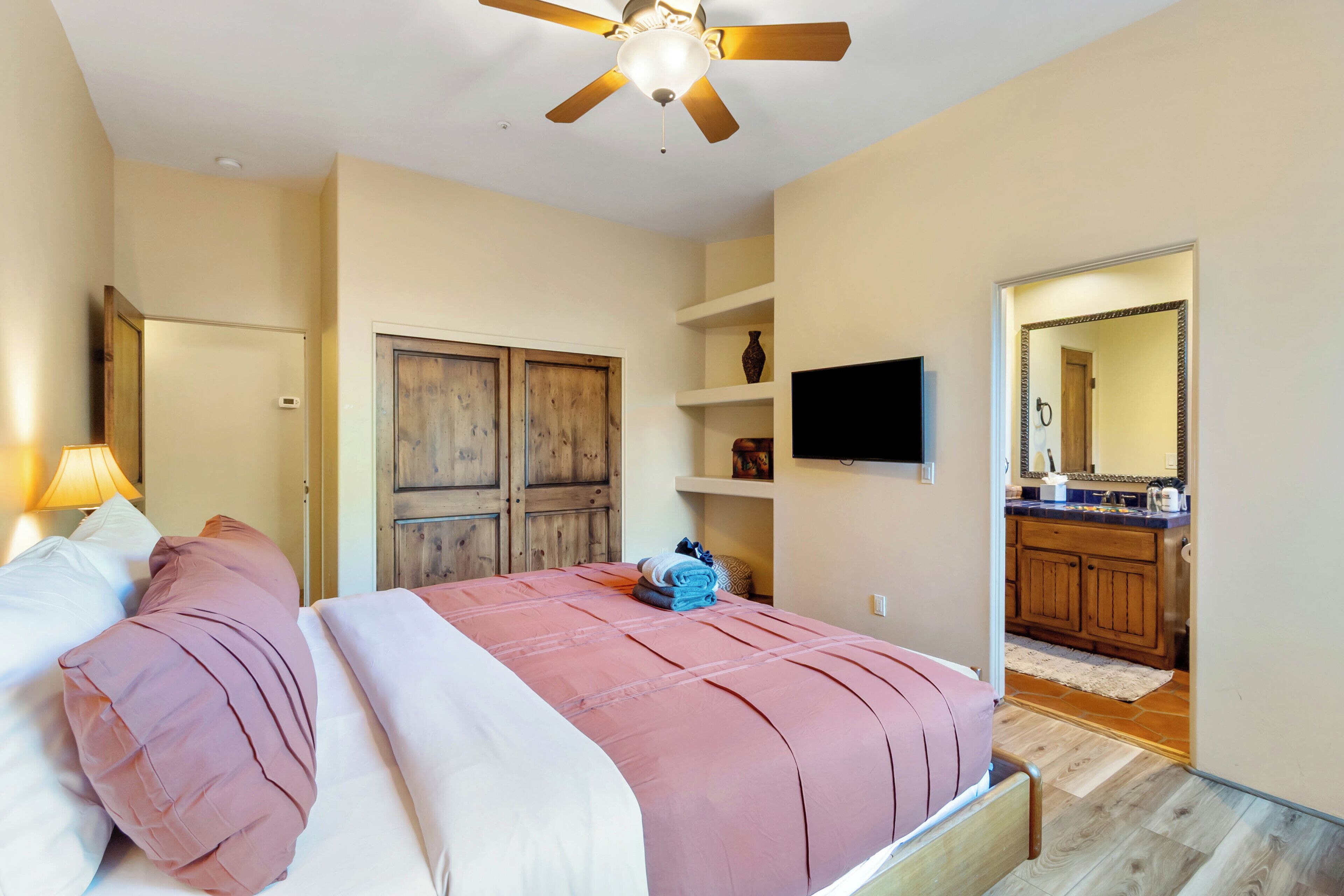 A bedroom with a bed, a ceiling fan, a TV, and a wooden wardrobe.