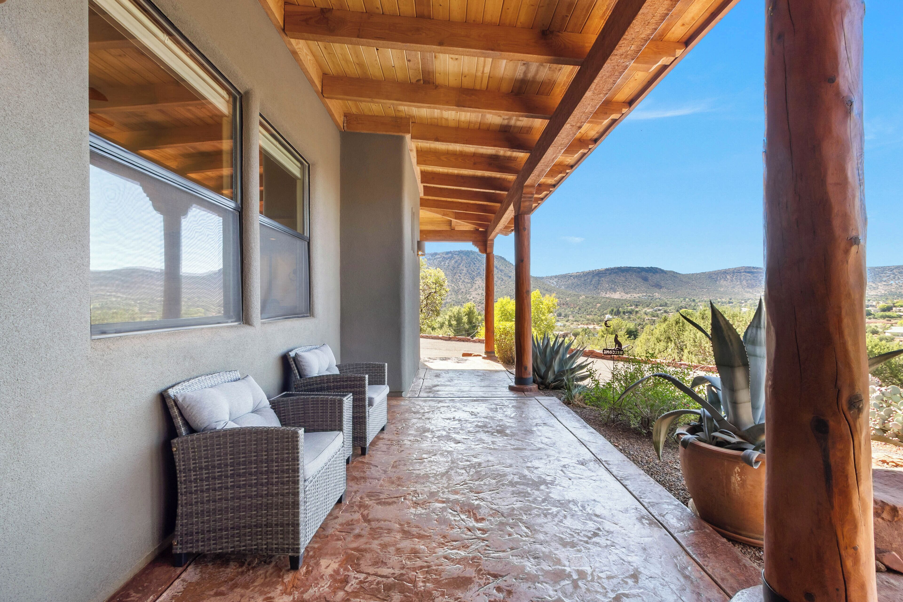 A covered patio with wicker furniture and a potted plant, overlooking a mountainous landscape.