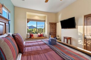Une chambre dotée d’un grand lit, d’un téléviseur fixé au mur et d’une fenêtre donnant sur les montagnes.