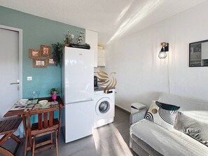 Un espace de vie compact comprenant un coin repas, un lave-linge, un canapé et une petite cuisine.