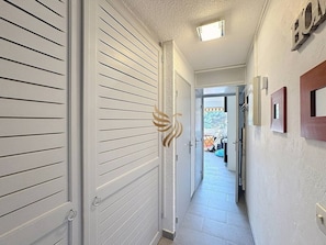 Corredor com portas brancas, uma luminária no teto e vista para área externa.