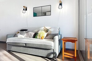 Un salon moderne avec un canapé gris, une table d’appoint en bois et une grande fenêtre.