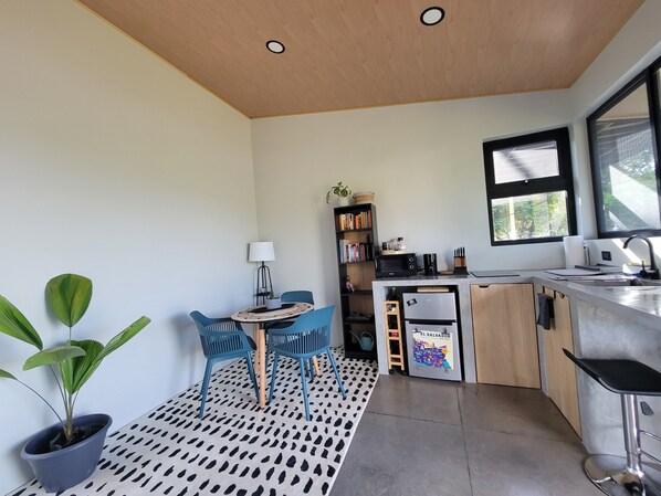 A compact kitchen with a dining area, a potted plant, and a bookshelf.