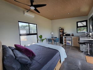 A modern bedroom with a bed, a desk, and a kitchenette.