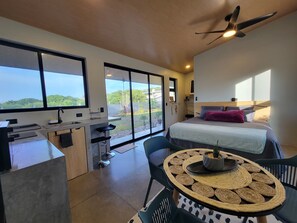 A modern bedroom with a large bed, a desk, and a balcony with a view.