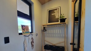 Un couloir avec une fenêtre, une porte, une étagère fixée au mur sur laquelle est posée une plante en pot, et un cadre contenant une citation inspirante.