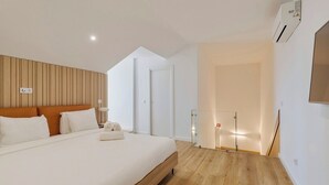 A modern bedroom with a wooden headboard, a large bed, a bedside table with a lamp, and a glass partition leading to a bathroom.